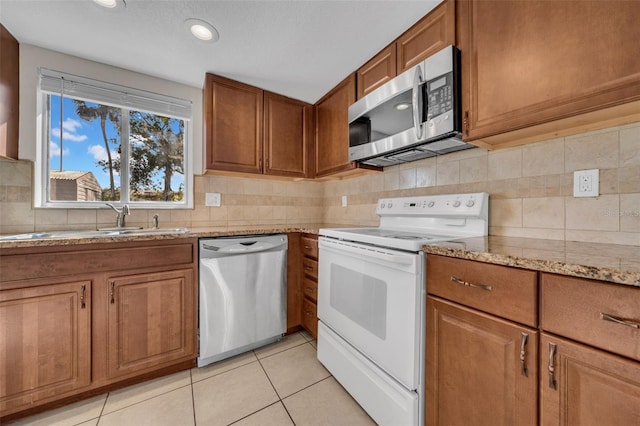 kitchen with light tile patterned floors, light stone countertops, appliances with stainless steel finishes, decorative backsplash, and brown cabinetry