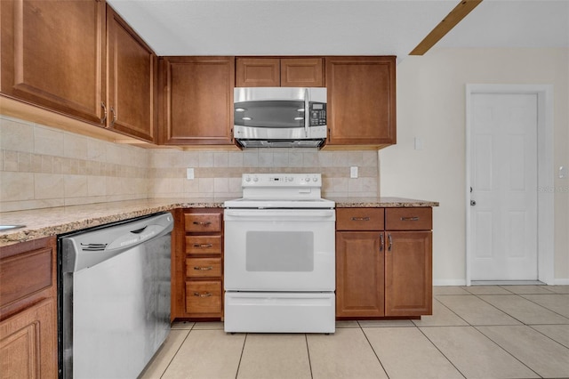 kitchen with light tile patterned floors, appliances with stainless steel finishes, backsplash, light stone countertops, and brown cabinetry