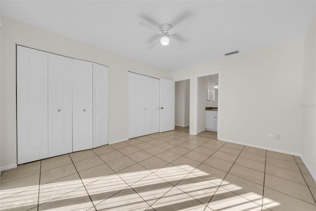 unfurnished bedroom featuring light tile patterned flooring, visible vents, baseboards, and two closets