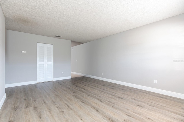 empty room with light wood-style floors, visible vents, a textured ceiling, and baseboards