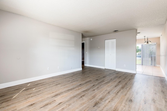 unfurnished room with visible vents, a textured ceiling, wood finished floors, a chandelier, and baseboards