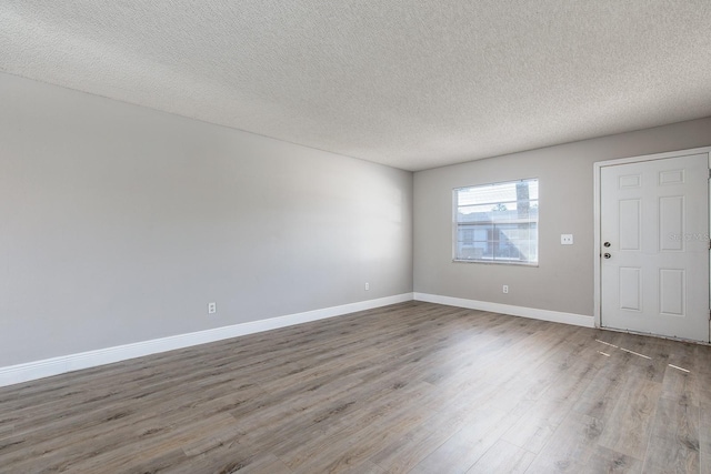 empty room with a textured ceiling, wood finished floors, and baseboards