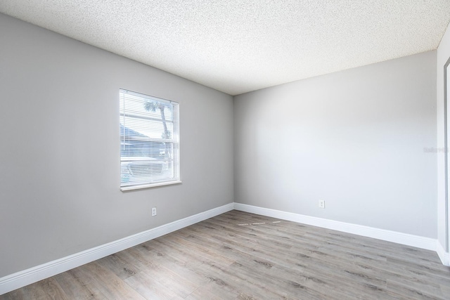 spare room with a textured ceiling, wood finished floors, and baseboards