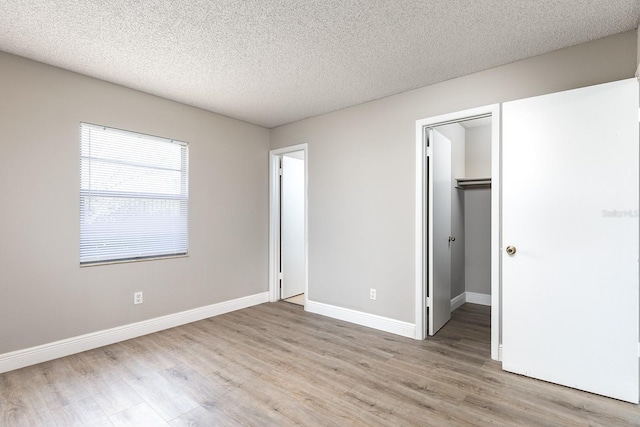 unfurnished bedroom with a textured ceiling, light wood-style flooring, baseboards, a closet, and a walk in closet