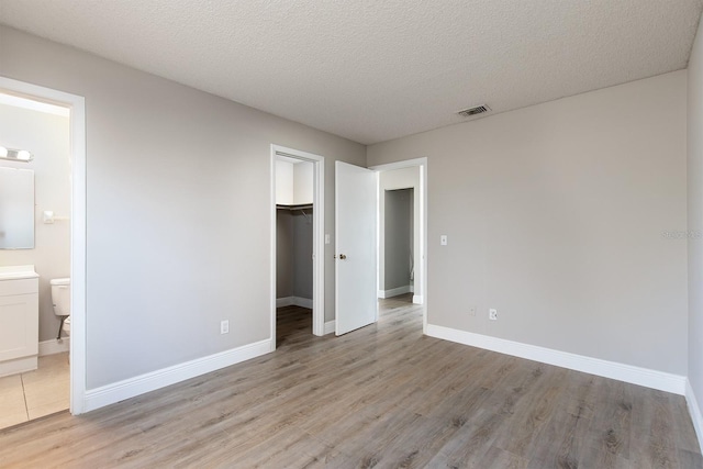 unfurnished bedroom featuring visible vents, a spacious closet, light wood-style floors, a textured ceiling, and baseboards