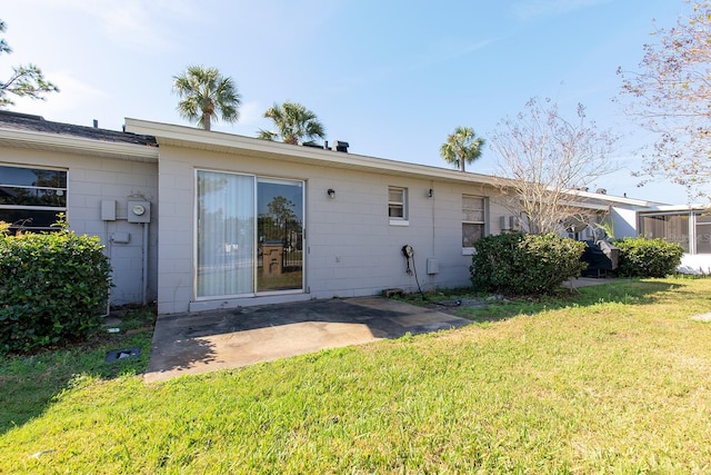 back of house with a lawn, a patio area, and concrete block siding