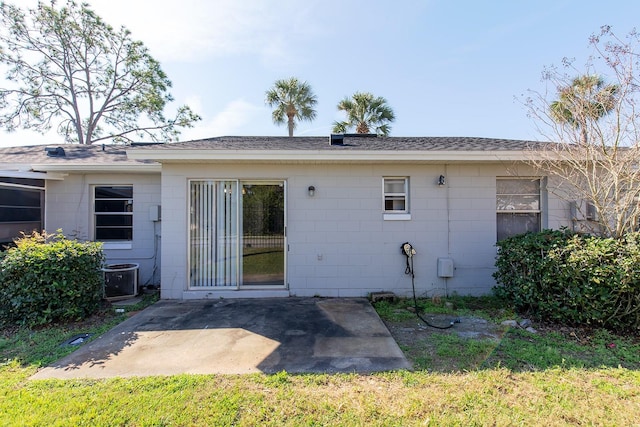 back of property with central air condition unit, concrete block siding, and a patio