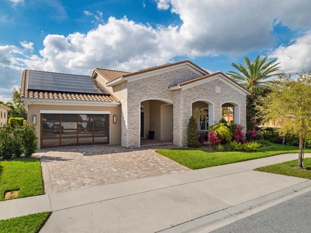 mediterranean / spanish-style house with a garage, solar panels, a tiled roof, decorative driveway, and a front yard