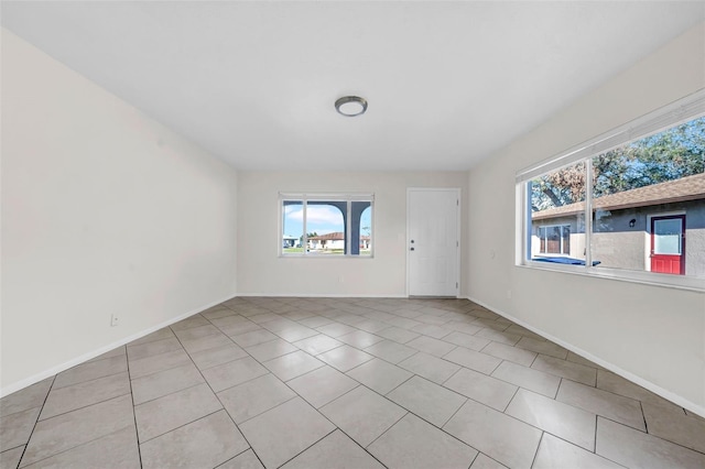 empty room featuring a healthy amount of sunlight, baseboards, and light tile patterned floors