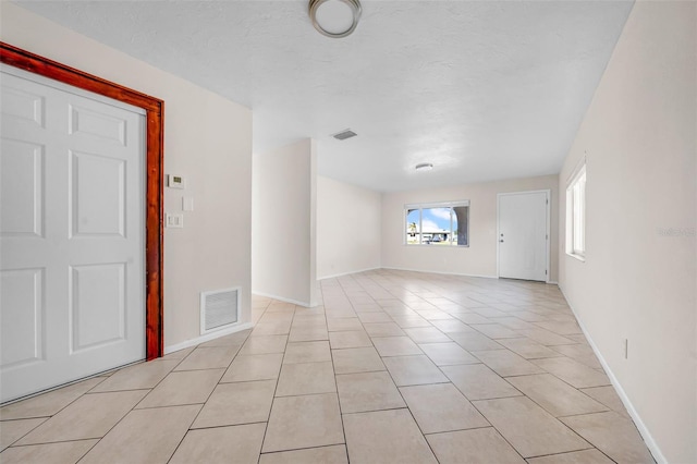 empty room featuring visible vents, a textured ceiling, baseboards, and light tile patterned floors