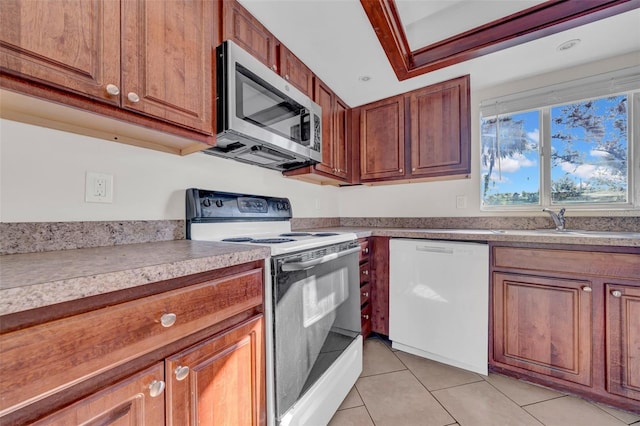 kitchen with brown cabinetry, white appliances, a sink, and light tile patterned floors