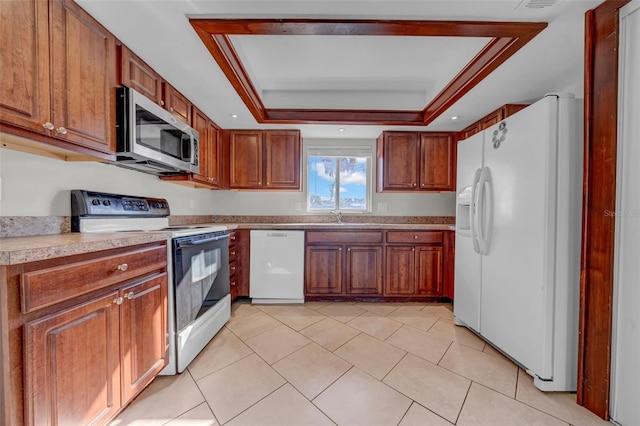 kitchen with brown cabinetry, a tray ceiling, and white appliances