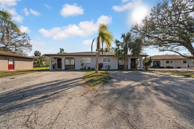 ranch-style home featuring gravel driveway and stucco siding