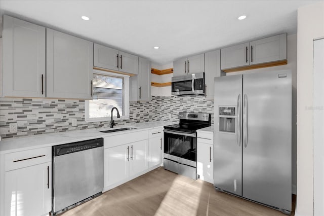 kitchen with stainless steel appliances, open shelves, light wood-type flooring, and a sink