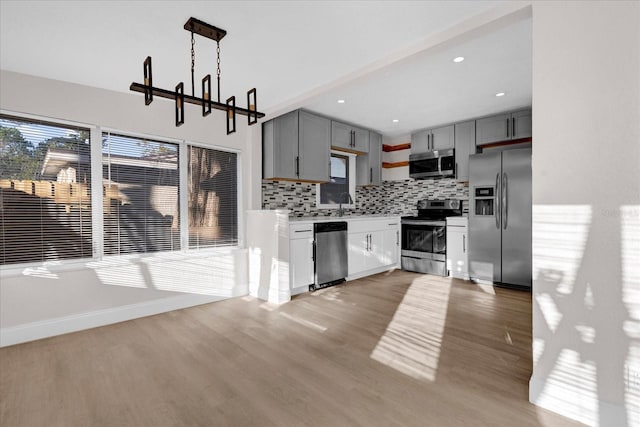 kitchen with stainless steel appliances, wood finished floors, backsplash, and gray cabinets