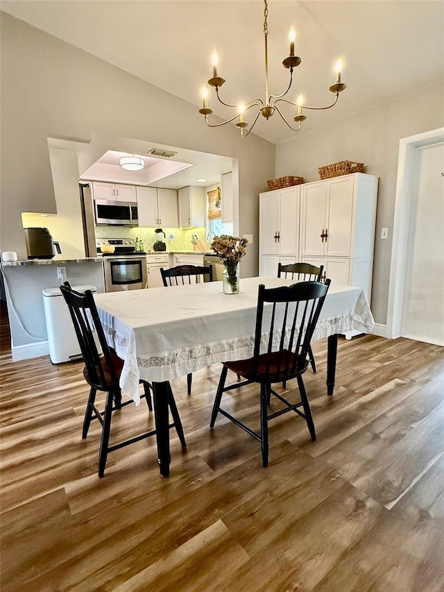 dining area featuring vaulted ceiling, baseboards, a chandelier, and wood finished floors