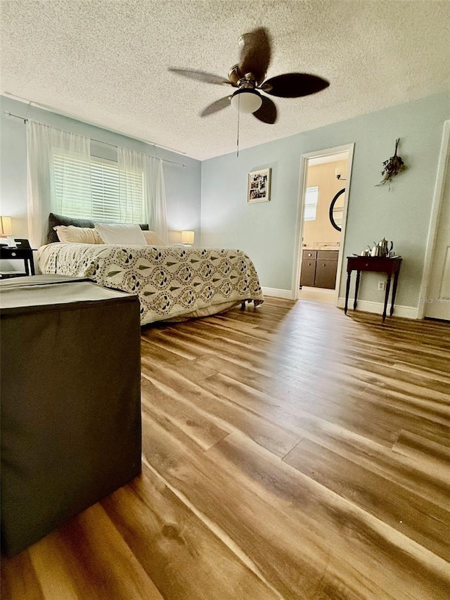 bedroom with a textured ceiling, multiple windows, wood finished floors, and baseboards