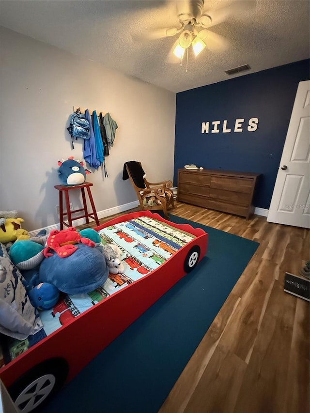 bedroom featuring a textured ceiling, wood finished floors, visible vents, and baseboards