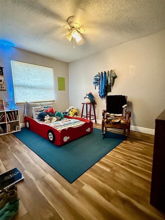 bedroom featuring a ceiling fan, a textured ceiling, baseboards, and wood finished floors