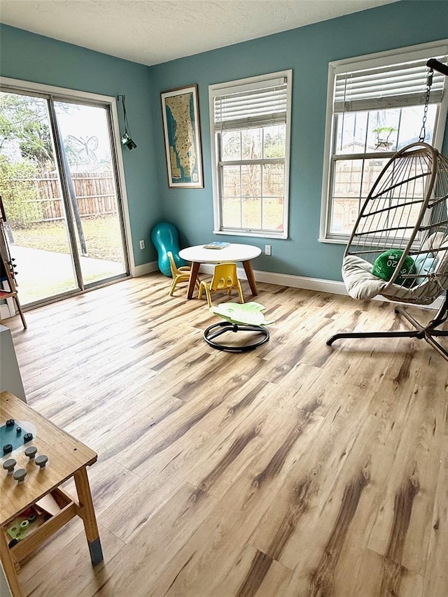 living area with a wealth of natural light, a textured ceiling, baseboards, and wood finished floors