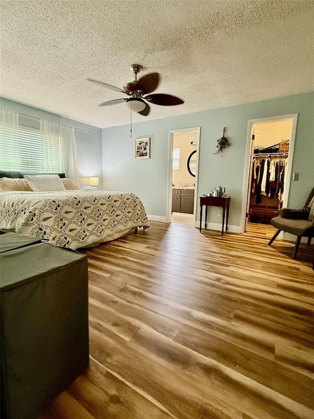 bedroom with a textured ceiling, wood finished floors, a walk in closet, and a ceiling fan