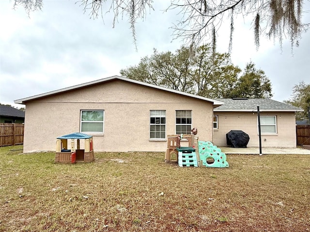 rear view of house with stucco siding, a patio, a lawn, and fence