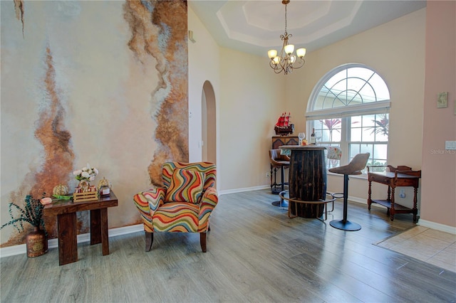 sitting room featuring arched walkways, a raised ceiling, wood finished floors, and a chandelier