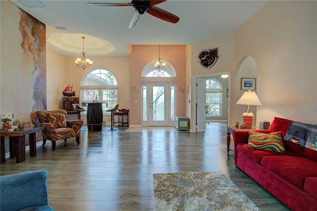 living area with ceiling fan with notable chandelier, wood finished floors, visible vents, baseboards, and a tray ceiling