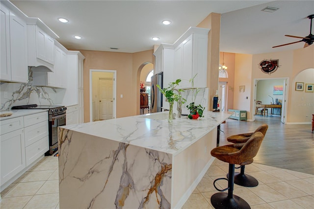 kitchen featuring arched walkways, light tile patterned floors, stainless steel appliances, visible vents, and backsplash