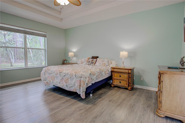 bedroom with ceiling fan, baseboards, a raised ceiling, and wood finished floors