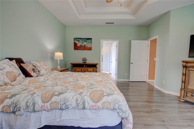 bedroom with baseboards, a tray ceiling, visible vents, and wood finished floors