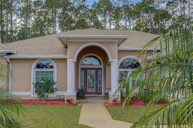 entrance to property with roof with shingles, a lawn, and stucco siding