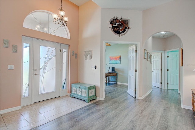 entrance foyer with a towering ceiling, light wood-style flooring, arched walkways, and baseboards