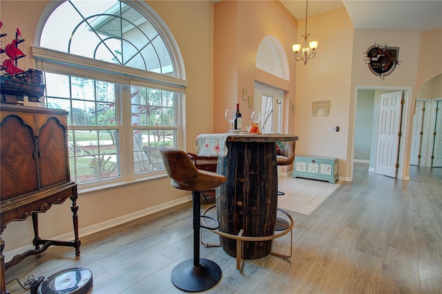 dining space with a chandelier, a towering ceiling, light wood-style flooring, and a bar