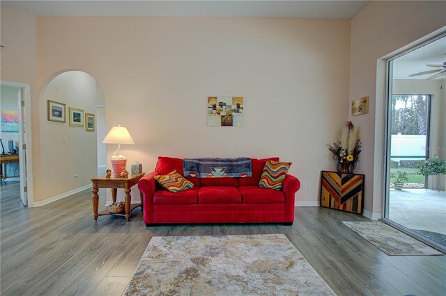 living area with arched walkways, ceiling fan, wood finished floors, and baseboards