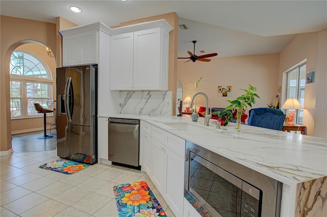 kitchen featuring light tile patterned floors, tasteful backsplash, appliances with stainless steel finishes, a peninsula, and a sink