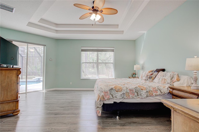 bedroom with access to exterior, visible vents, a tray ceiling, and wood finished floors