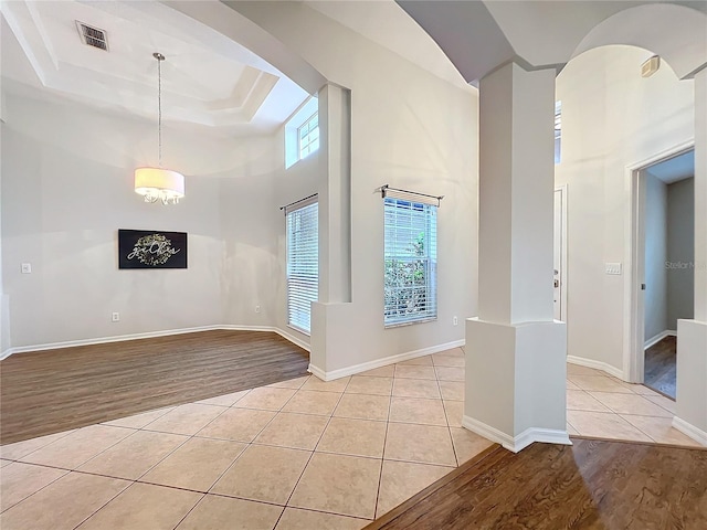 unfurnished room featuring a tray ceiling, visible vents, a towering ceiling, light tile patterned flooring, and baseboards