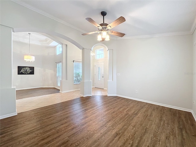 empty room featuring arched walkways, ornamental molding, wood finished floors, and baseboards