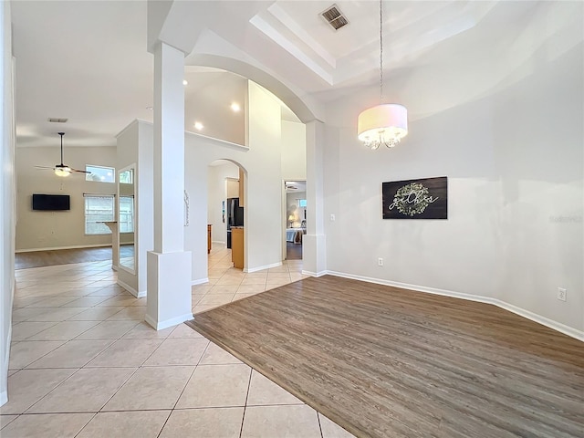 unfurnished room with light tile patterned floors, a high ceiling, visible vents, and arched walkways