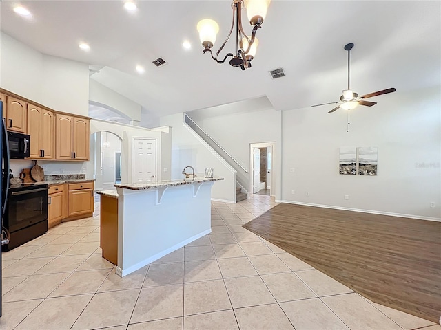 kitchen featuring light tile patterned floors, arched walkways, visible vents, black appliances, and a kitchen bar