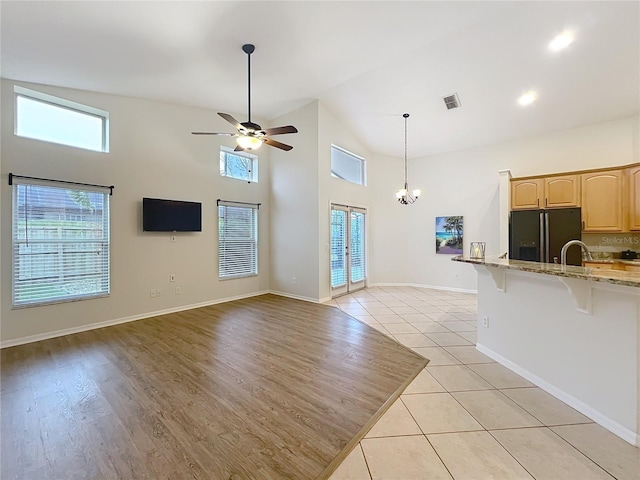 unfurnished living room featuring visible vents, baseboards, light tile patterned flooring, high vaulted ceiling, and ceiling fan with notable chandelier