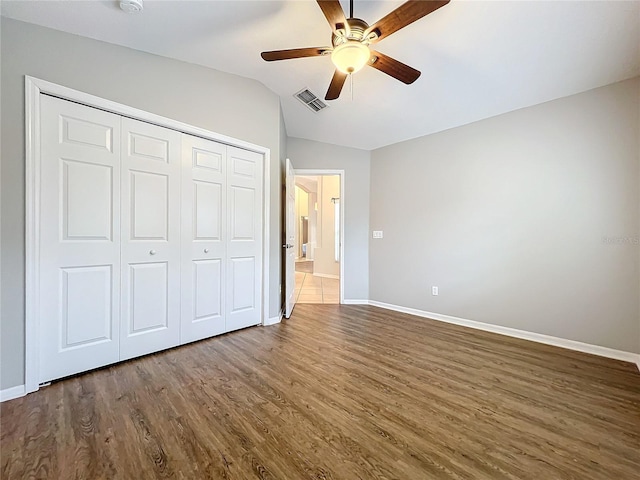 unfurnished bedroom featuring baseboards, visible vents, dark wood-style flooring, vaulted ceiling, and a closet