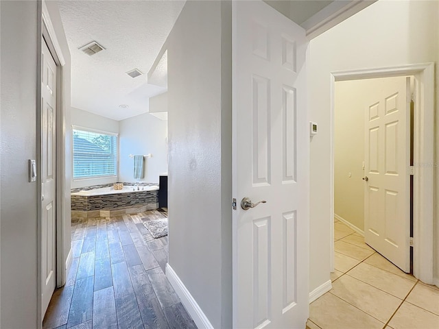 corridor featuring light wood-type flooring, baseboards, visible vents, and a textured ceiling