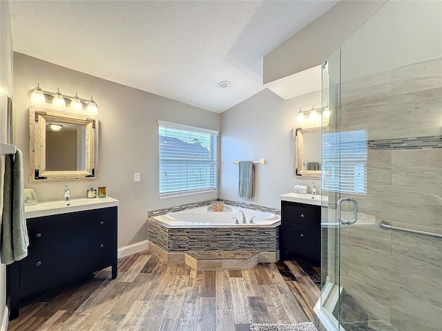 full bath with a garden tub, wood finished floors, two vanities, vaulted ceiling, and a stall shower