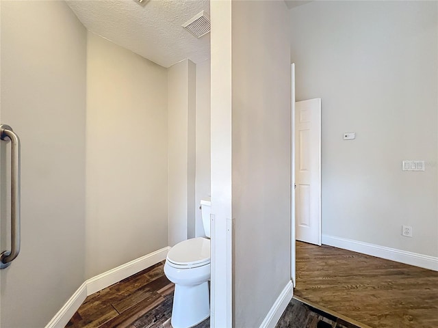 bathroom featuring a textured ceiling, toilet, wood finished floors, visible vents, and baseboards