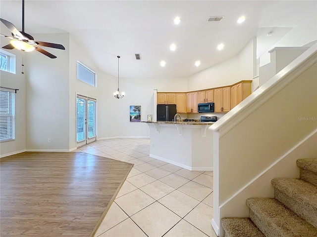 kitchen featuring open floor plan, a kitchen breakfast bar, light brown cabinetry, black appliances, and light tile patterned flooring