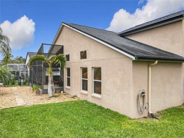 rear view of house with roof with shingles, glass enclosure, a lawn, and stucco siding