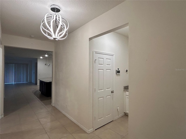 hallway with baseboards, a chandelier, a textured ceiling, and light tile patterned flooring