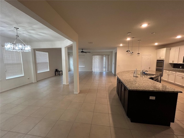 kitchen with white cabinets, light stone counters, open floor plan, a sink, and ceiling fan with notable chandelier